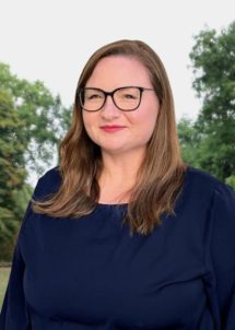 Customer Service Manager from WCID No. 17 standing outdoors near trees, wearing business attire and smiling at the camera.